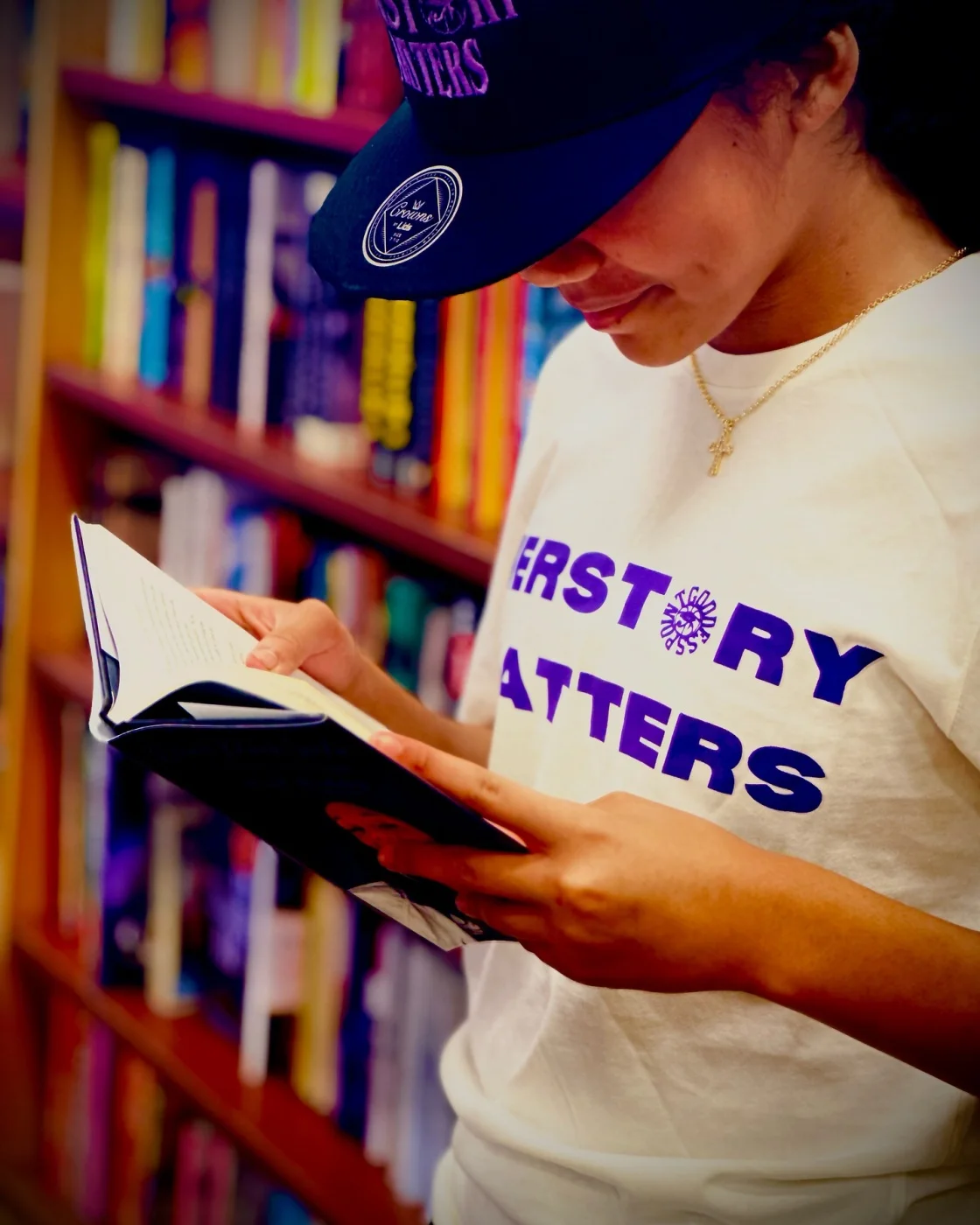 Student reading in a library wearing a HERSTORY MATTERS hat and tee