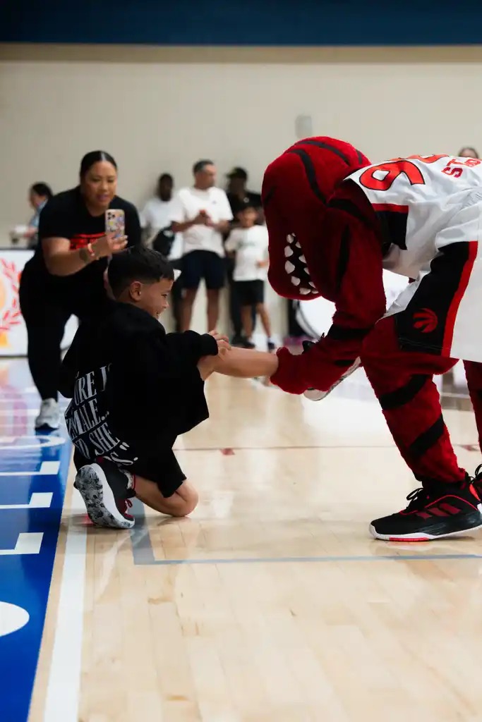 A young player high-fiving the Toronto Raptors mascot at a Point Goddess event