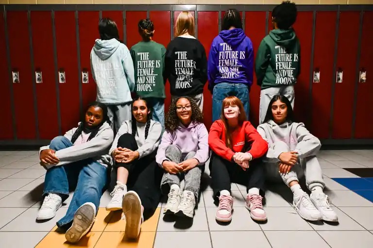 Point Goddess athletes in THE FUTURE IS FEMALE hoodies sitting together in front of school lockers