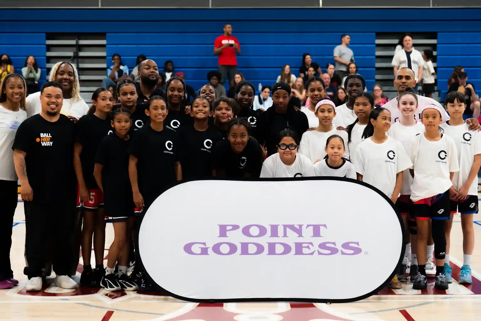Point Goddess athletes, coaches and mentors gathered around the Point Goddess banner at centre court