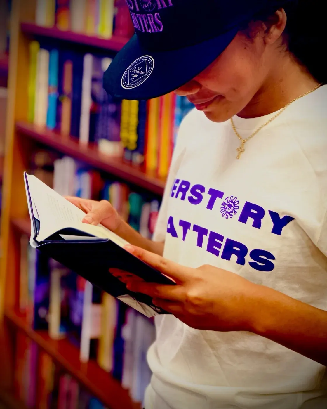Student reading in a library wearing a HERSTORY MATTERS hat and tee