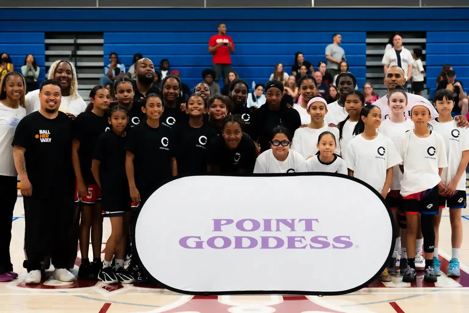 Point Goddess athletes, coaches and mentors gathered around the Point Goddess banner at centre court